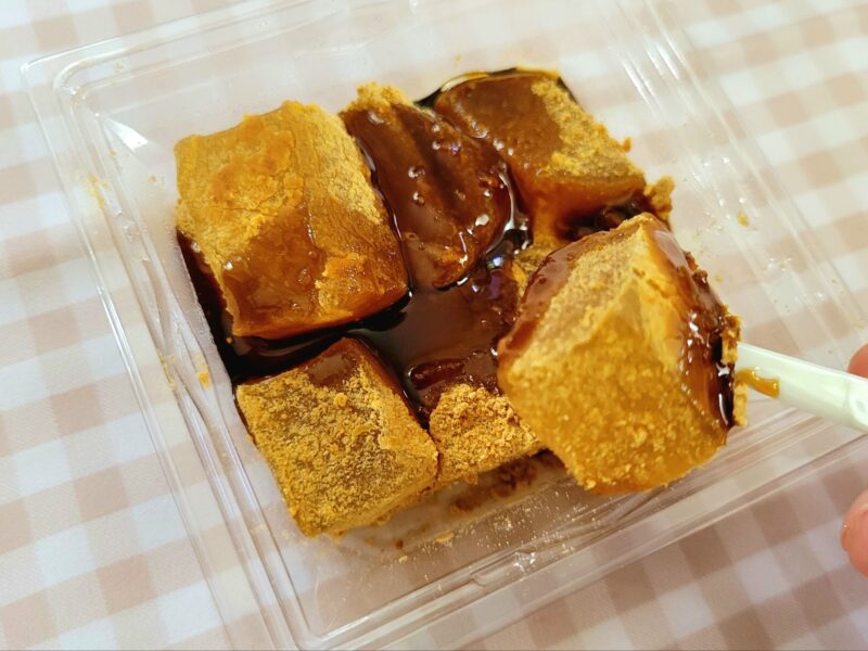 黒蜜がかかった名水わらび餅を菓子楊枝で持ち上げた様子